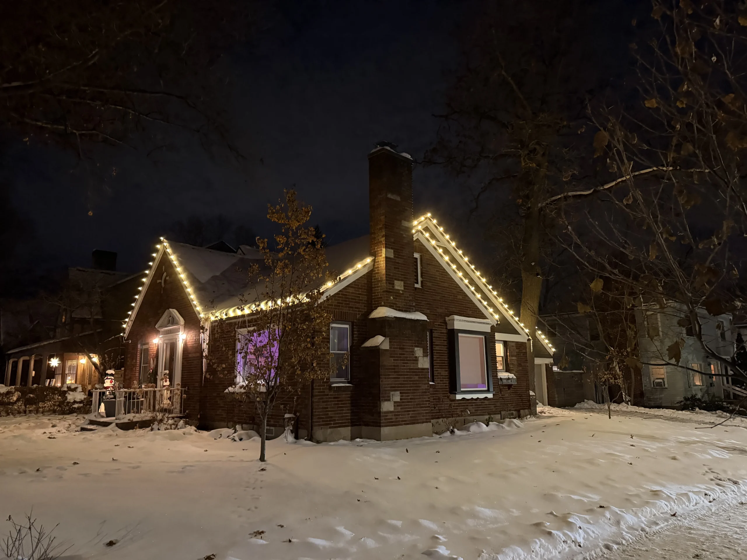 Christmas light installation in West Michigan - brick cottage with warm white roofline lights on a snowy night