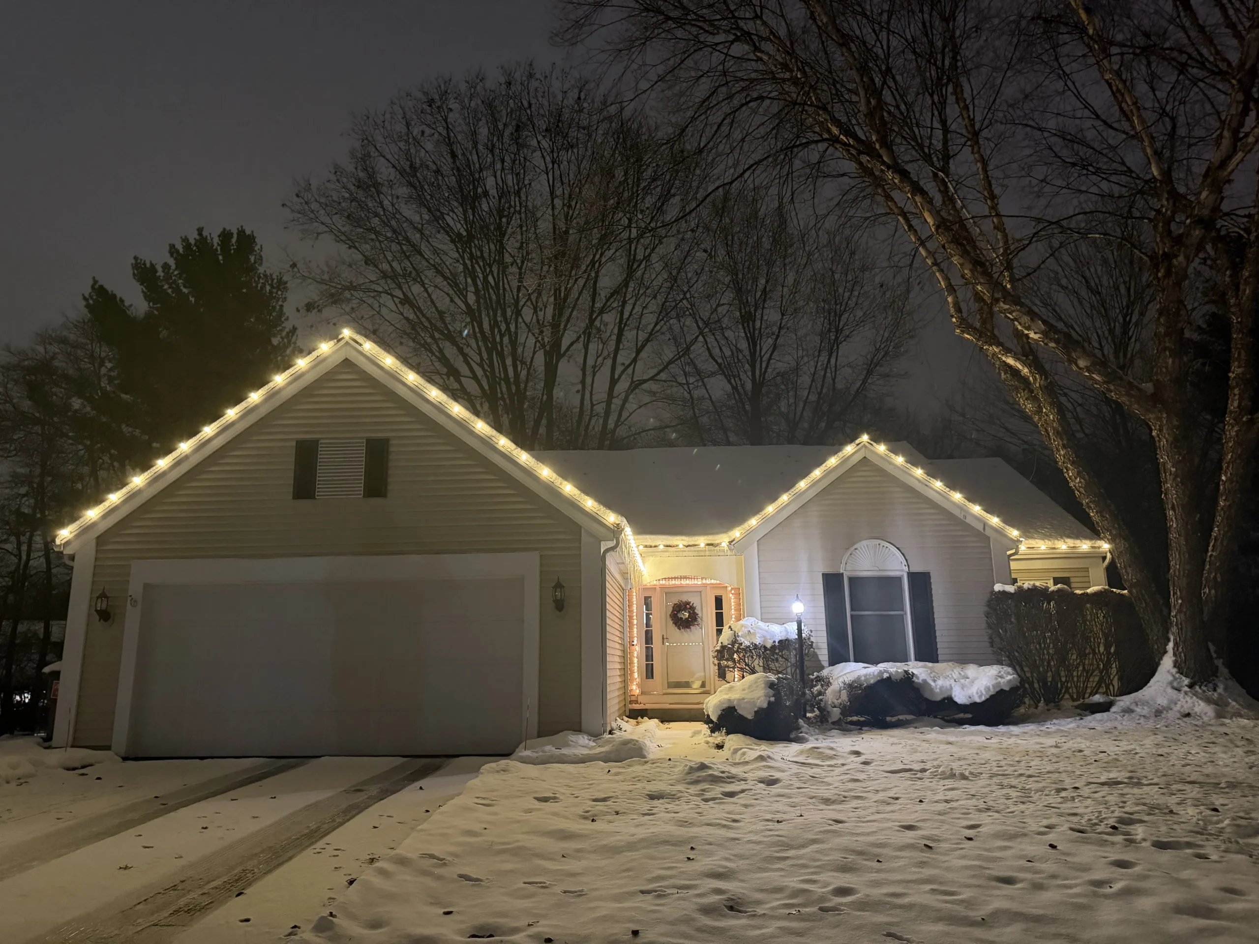 Christmas light installation in West Michigan - home with warm white roofline lights in fresh snow at night