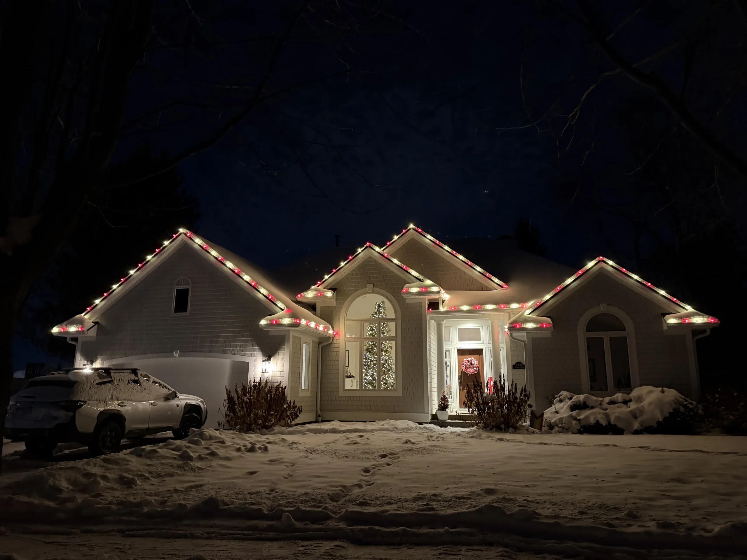 Christmas light installation in West Michigan - home with red and white roofline lights on a snowy night