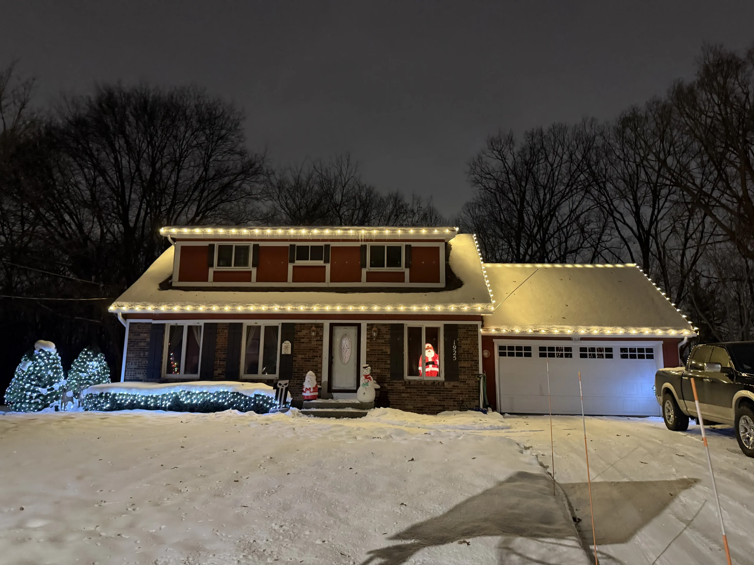 Christmas light installation in West Michigan - two-story brick home with warm white roofline lights in snow