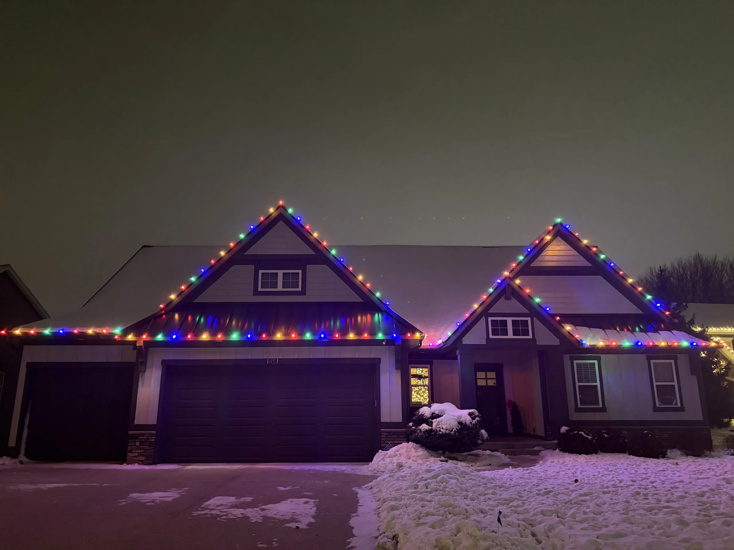 Christmas light installation in West Michigan - home with multicolor roofline lights on a snowy night