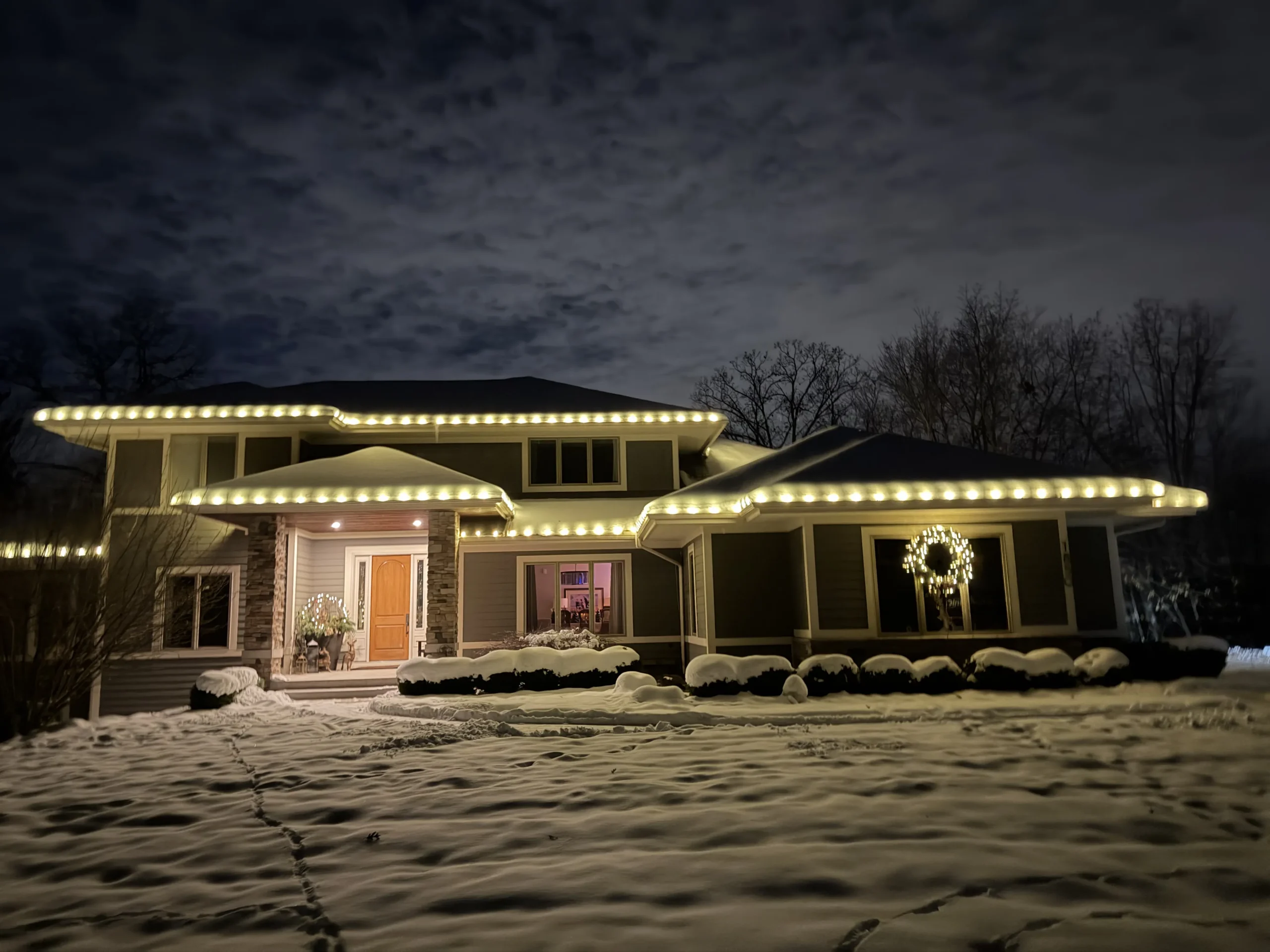 Christmas light installation in East Grand Rapids, Michigan - snowy home with white roofline lights and wreath