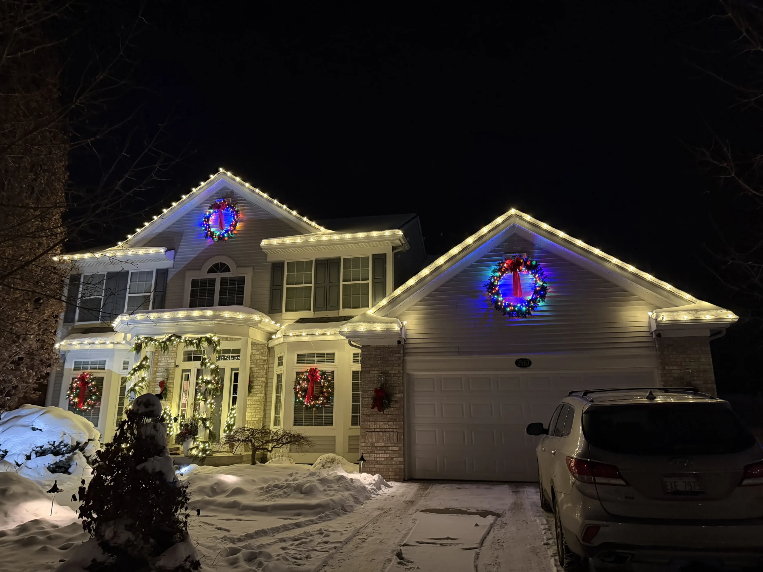 Christmas light installation in East Grand Rapids, Michigan - home with white roofline lights and lit wreaths